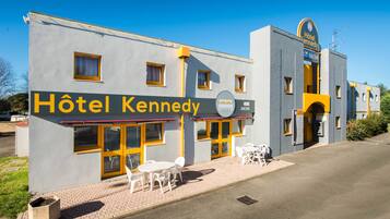 A building with a sign reading "Hôtel Kennedy" and a 24/24 service indication. There are outdoor tables and chairs.