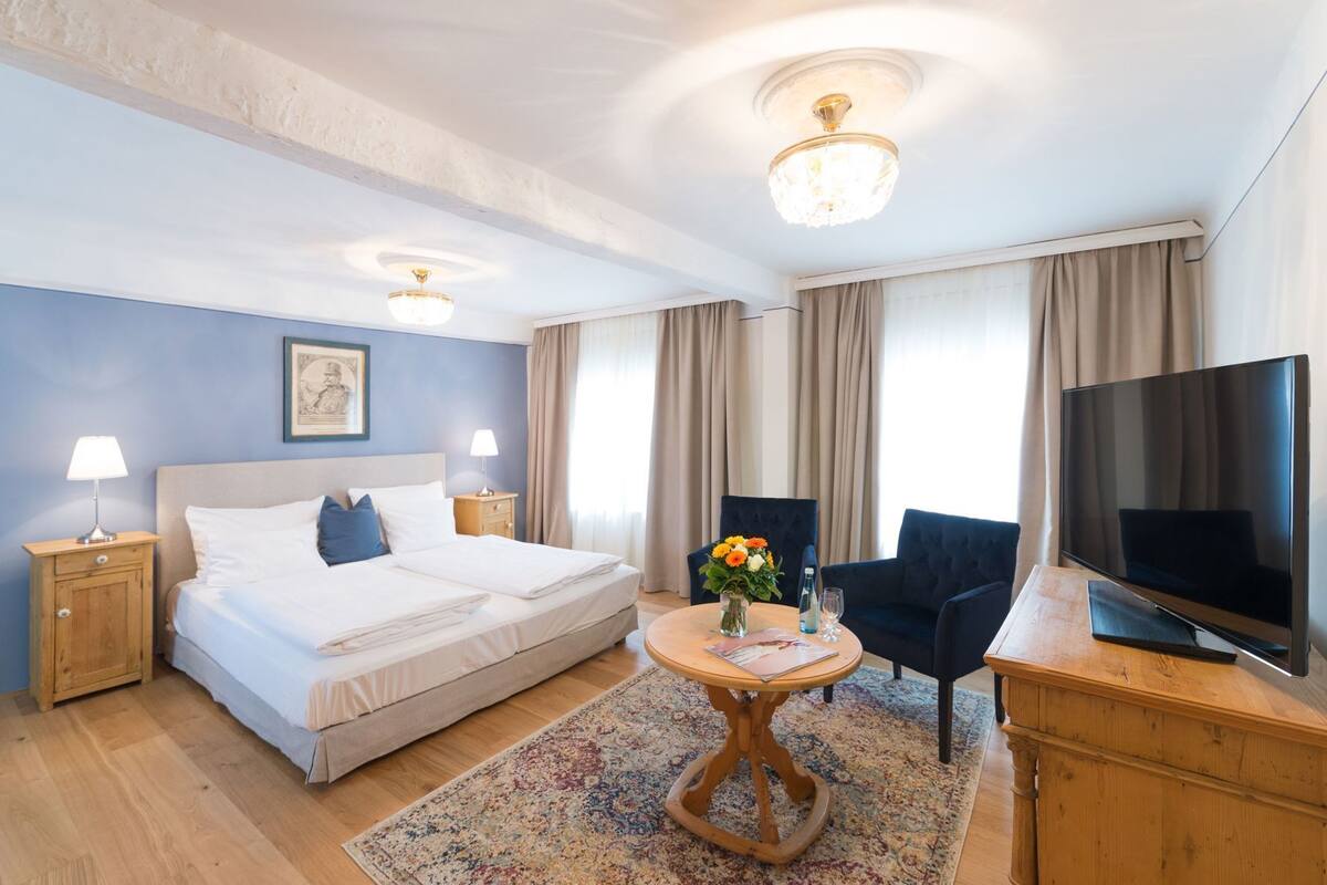 A hotel room with a bed, a TV, a desk, a chair, and a window with curtains.