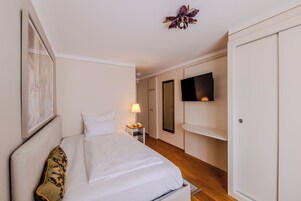 Habitación de hotel con cama, mesita de noche con lámpara, televisor montado en la pared y armario.