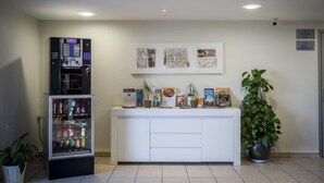 A reception area with a vending machine, a counter with informational brochures, and a potted plant. - Adams Hotel (Metz)