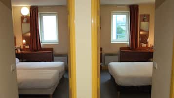 Een hotelkamer met spiegels, twee bedden, een raam, een nachtkastje en een lamp.