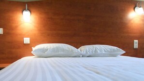 A neatly made bed with white linens and two pillows, a wooden headboard, and two wall-mounted light fixtures. - Adams Hotel (Metz)