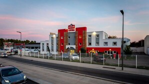 A modern hotel with a red and white facade, multiple floors, and a parking area in front. - Adams Hotel (Metz)