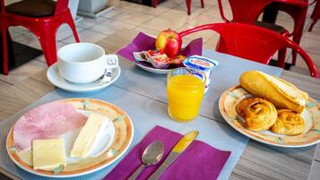 En frukostuppläggning med tallrikar fyllda med skinka, ost, bröd och bakverk, ett glas apelsinjuice och en kopp kaffe.