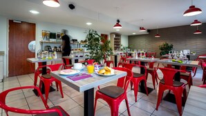 A modern restaurant with red chairs and tables, a kitchen area, and hanging red pendant lights. - Adams Hotel (Metz)