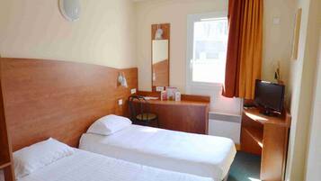 A hotel room with two single beds, a desk with a chair, a television, and a window with curtains.