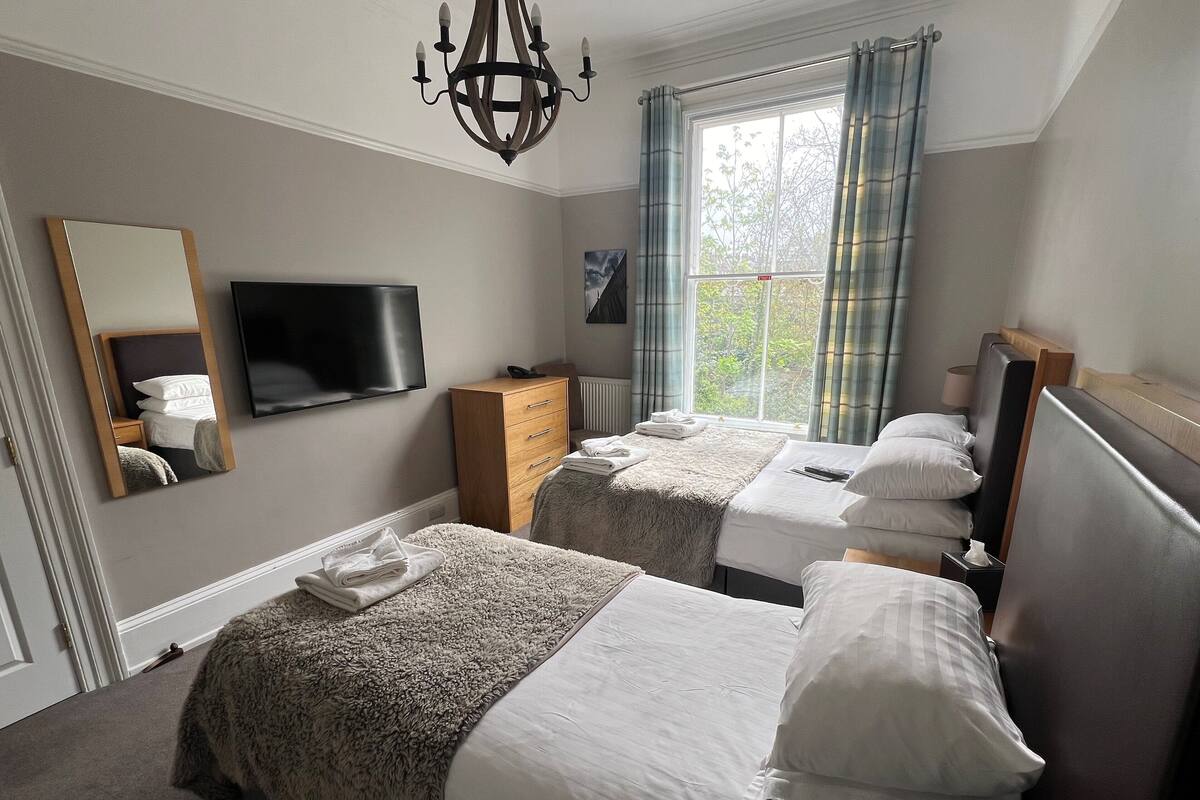 A hotel room with two beds, a TV, a dresser, and a window with curtains.