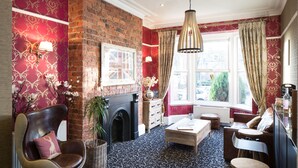 A cozy room with a fireplace, comfortable seating, a coffee table, and a view of the street through large windows. - Hedley House Hotel Wellness and Spa (York)
