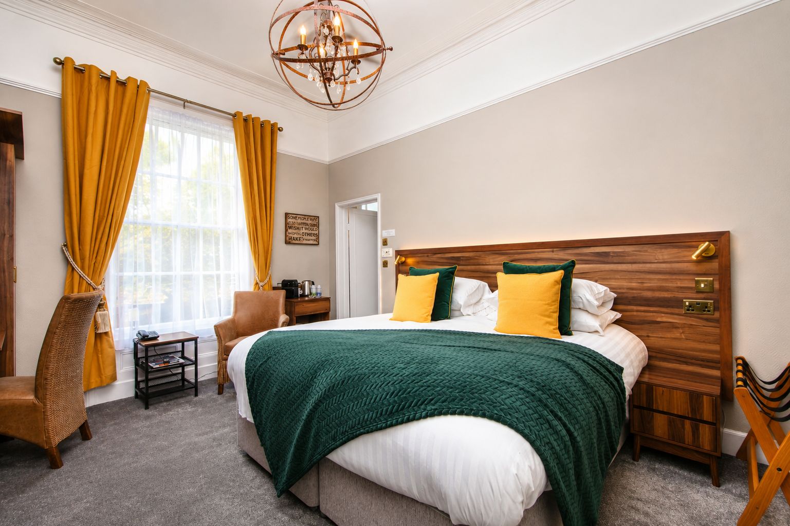 Ein Hotelzimmer mit einem großen Bett, einem Holzkopfende, einem Nachttisch, einem Sessel, einem kleinen Tisch und einer Kristallleuchtre.