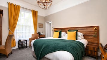 A hotel room with a large bed, a wooden headboard, a nightstand, a chair, a small table, and a chandelier.