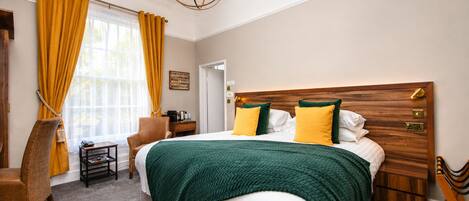 Ein Hotelzimmer mit einem großen Bett, einem Holzkopfende, einem Nachttisch, einem Sessel, einem kleinen Tisch und einer Kristallleuchtre.