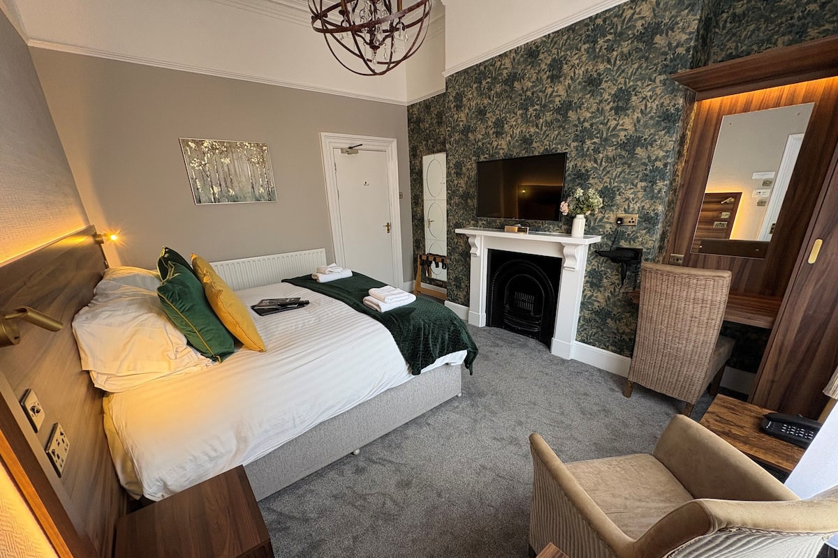 A bedroom with a bed, a chair, a fireplace, and a mirror.