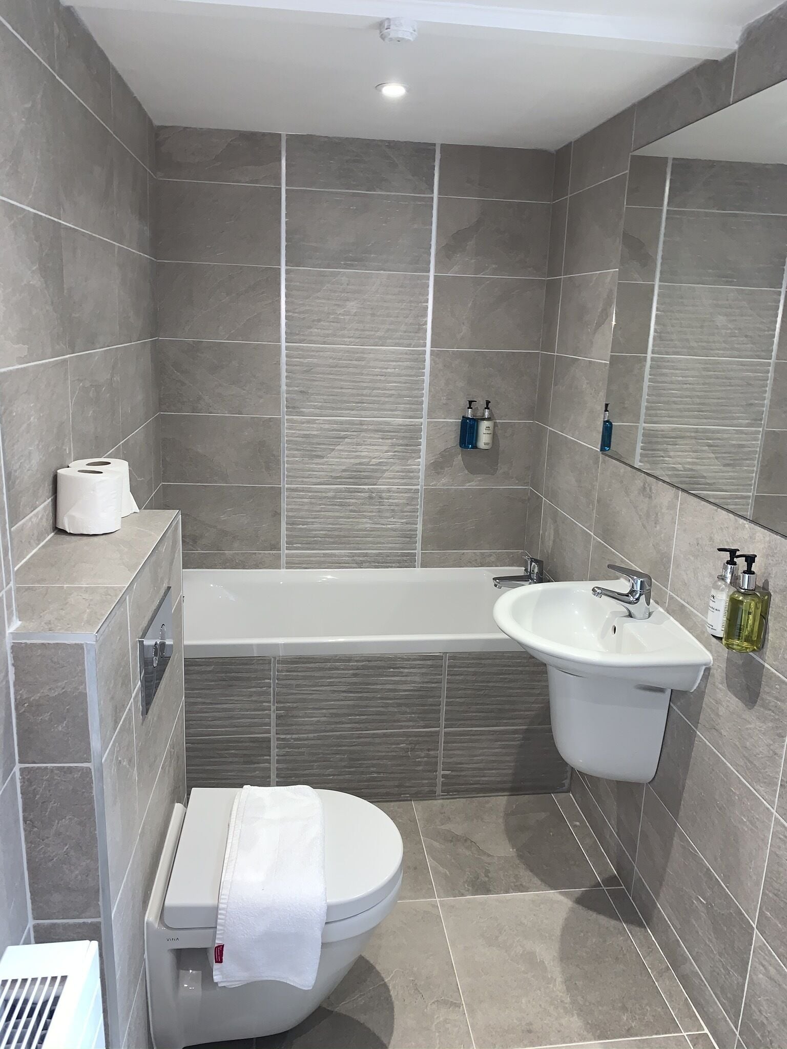 A modern bathroom with a bathtub, sink, toilet, and a mirror.