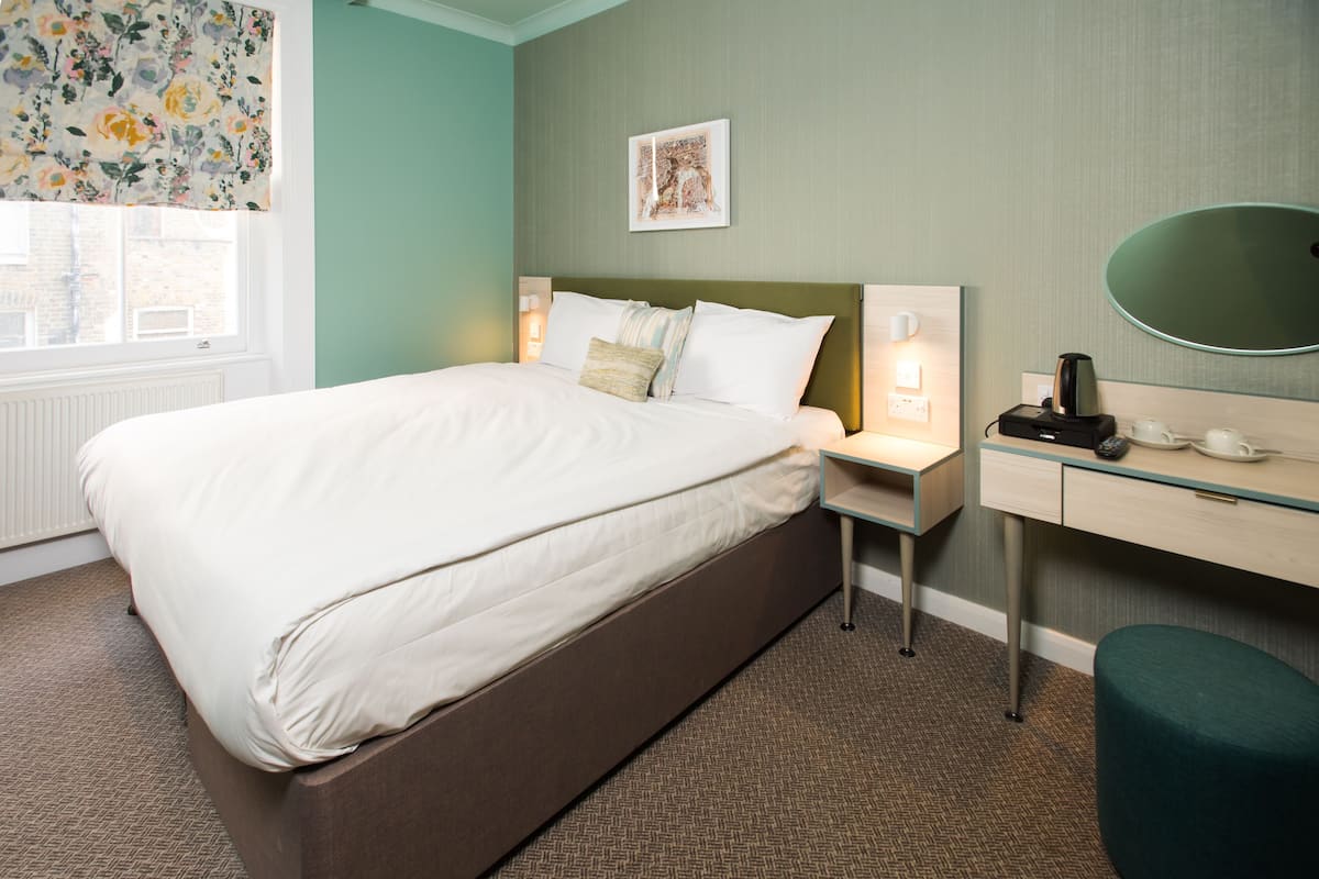 Une chambre d’hôtel avec un grand lit, des tables de chevet, un bureau avec un miroir et une fenêtre donnant sur des immeubles.
