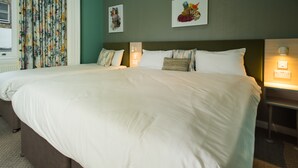 A large bed with white linens, a headboard, and two bedside tables with lamps. - Caring Hotel (London)