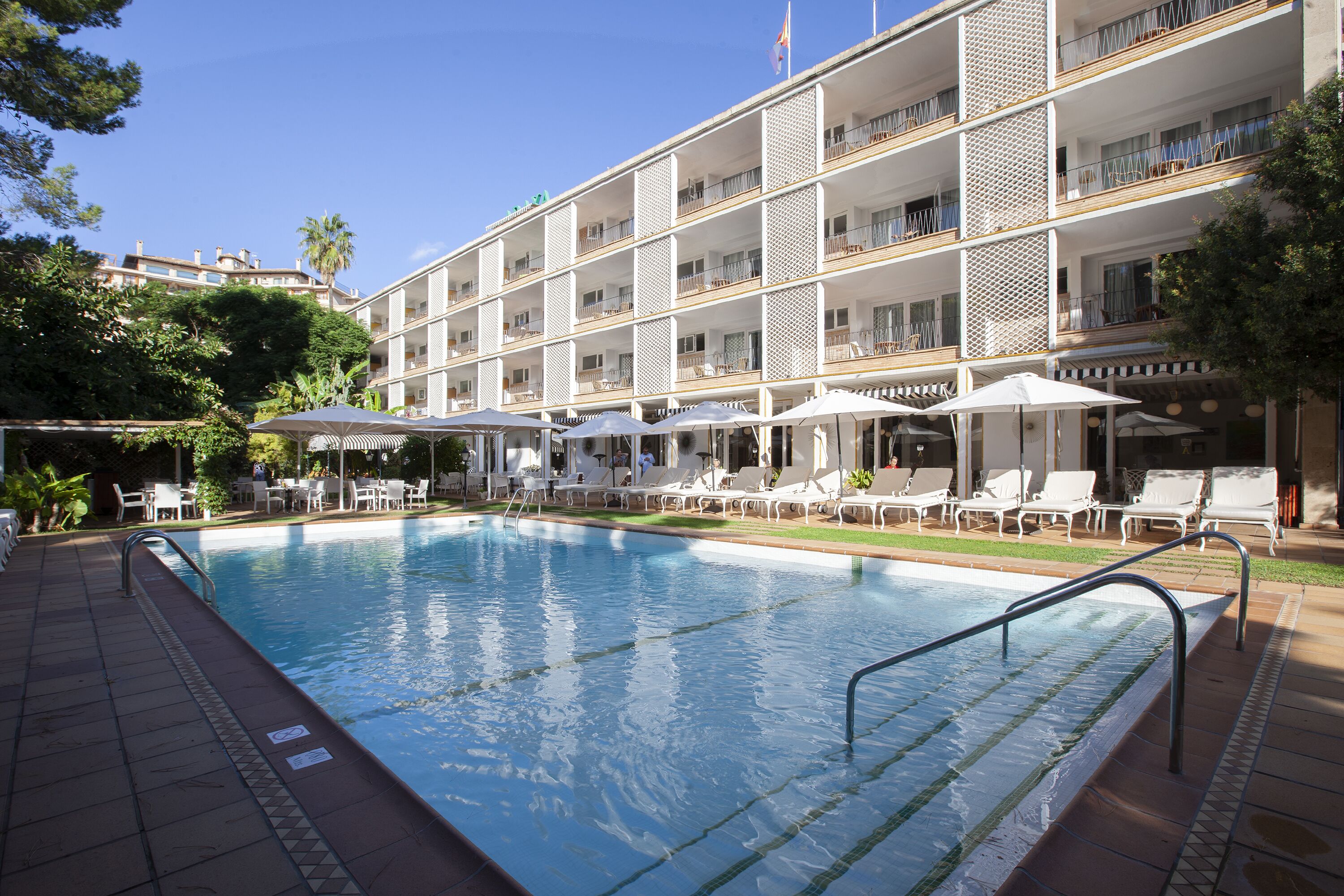 A hotel with a swimming pool, lounge chairs, and umbrellas.
