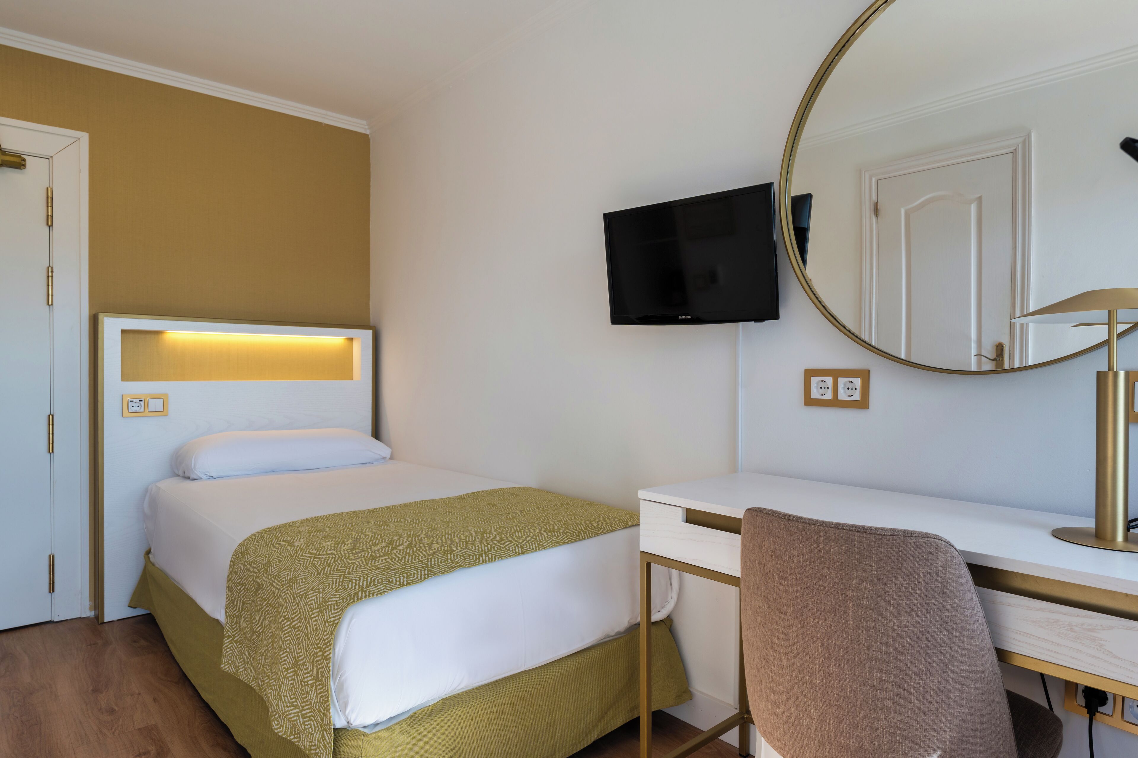 A hotel room with a bed, desk, chair, TV, and mirror.