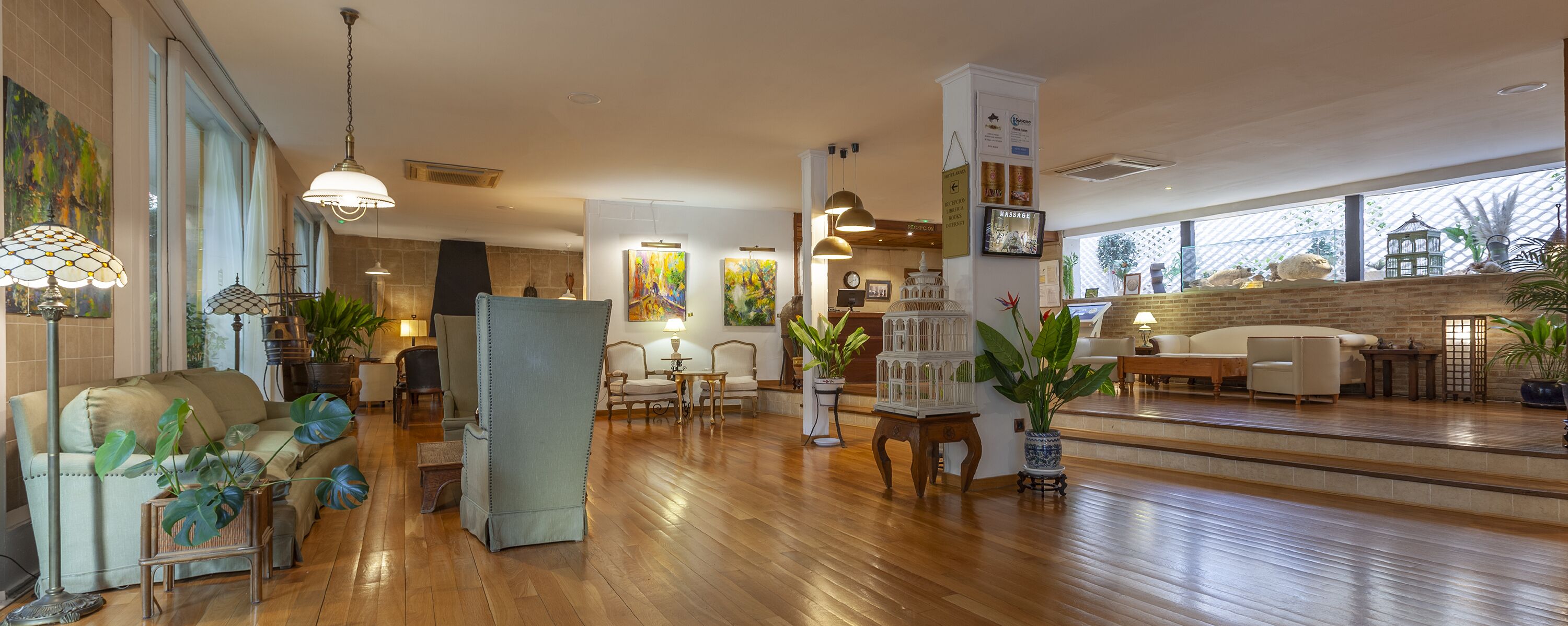 A spacious lobby with wooden flooring, a variety of seating options including sofas and chairs, and several potted plants.