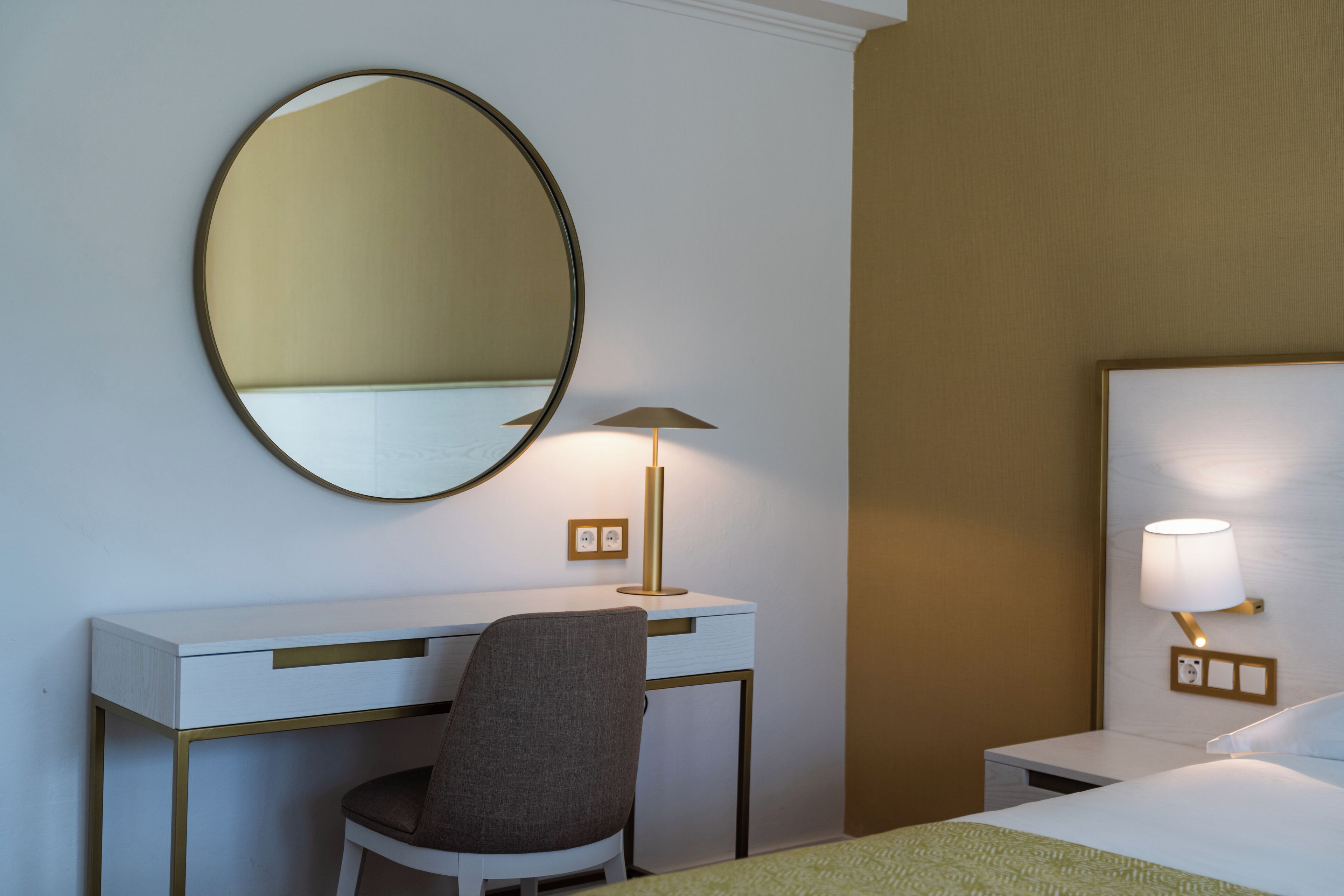 Habitació d'hotel amb escriptori, cadira, llit i làmpada fixada a la paret.