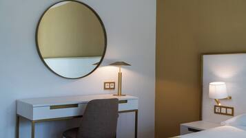 Habitació d'hotel amb escriptori, cadira, llit i làmpada fixada a la paret.