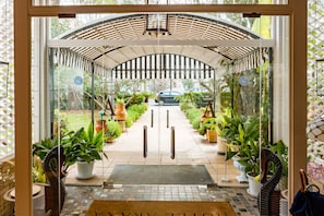 Entrada de hotel con puerta de vidrio, un toldo y plantas en macetas.