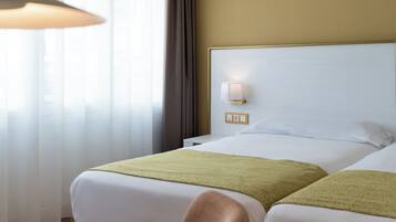 A hotel room with two beds, a nightstand, a lamp, and a window with curtains.