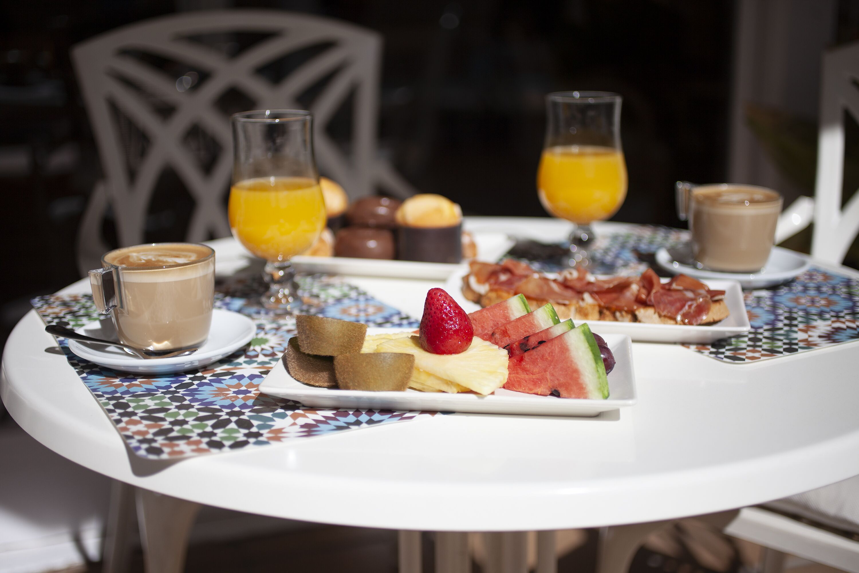 A breakfast table with a variety of food items and drinks, including a plate of toast, fruit, and a slice of cake, along with two glasses of orange juice and two cups of coffee.