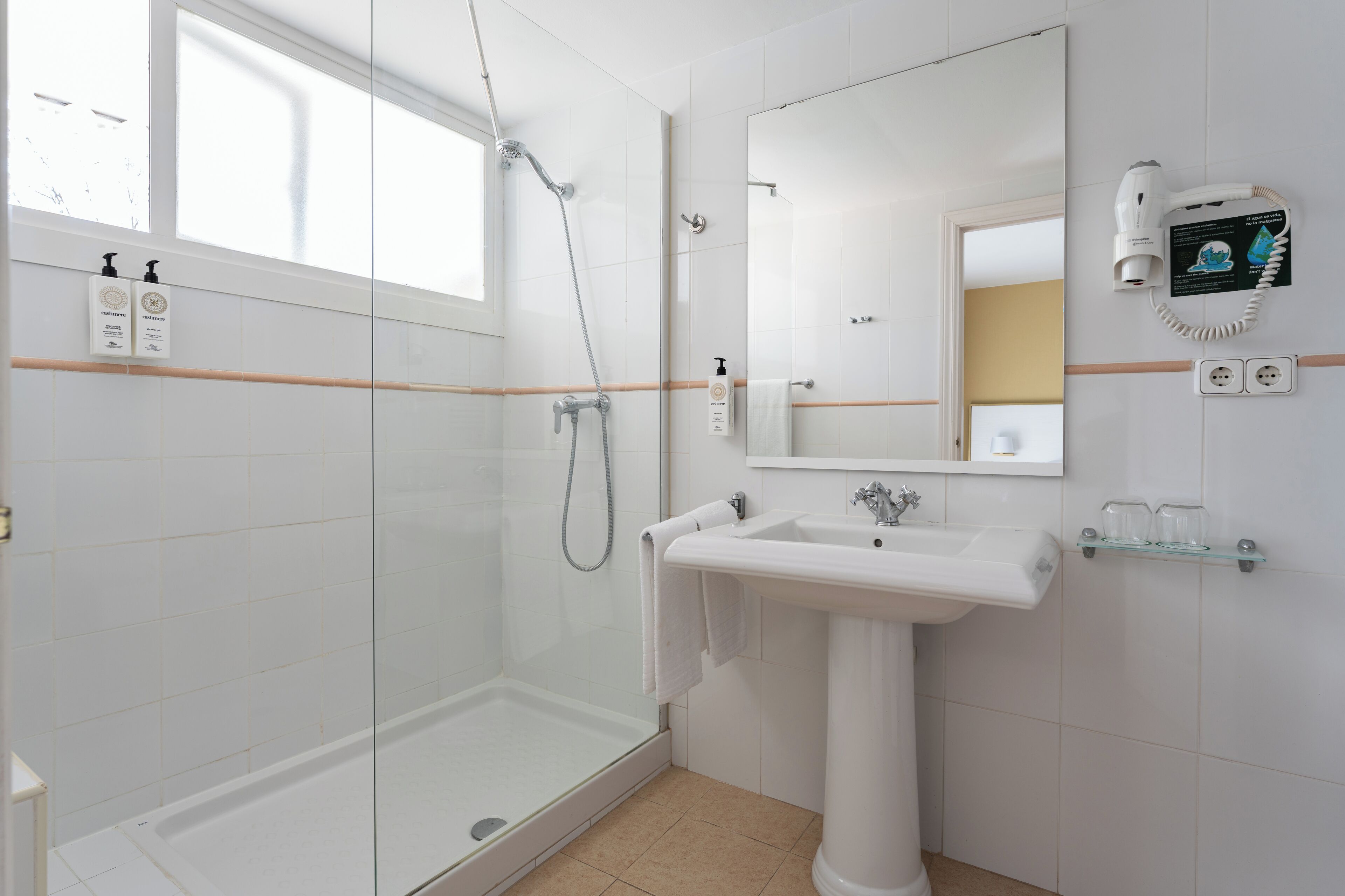 Un baño moderno con cabina de ducha de vidrio, lavabo pedestal y un espejo grande.