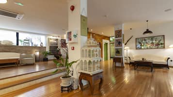 A hotel lobby with wooden flooring, a reception desk, a white sofa, and a staircase leading to another floor.