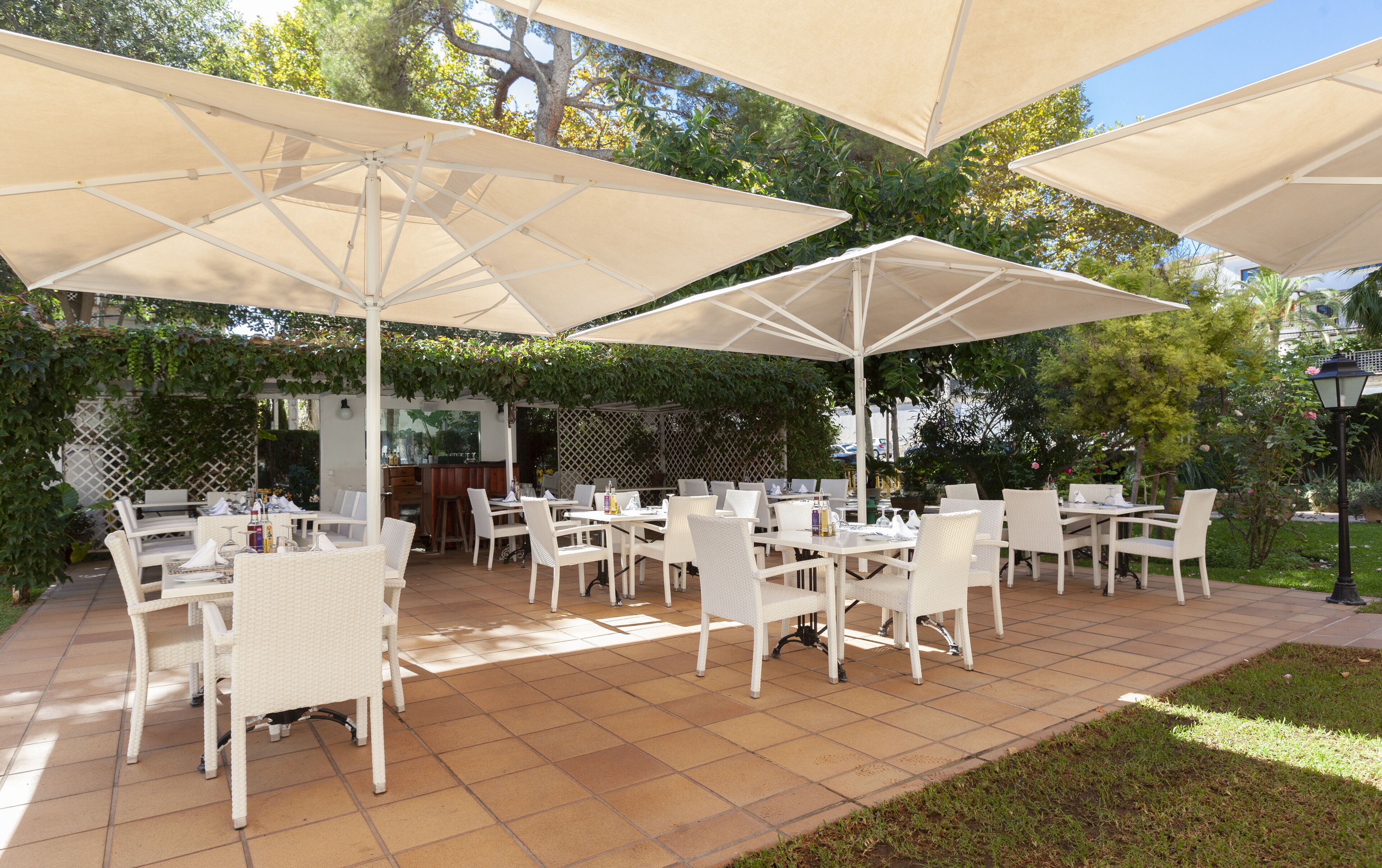 An outdoor patio area with white wicker furniture and large beige umbrellas.