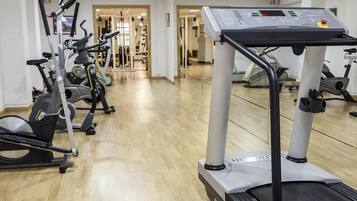 Une salle de sport équipée de machines de cardio, dotée d’un mur miroir et d’un plancher en bois.