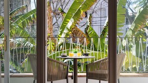A dining area with a table set for two, surrounded by wicker chairs, with a view of tropical foliage through a glass door. - Hotel Araxa - Adults Only (Palma de Mallorca)
