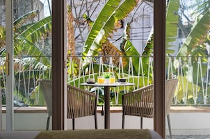 Un coin repas avec une table dressée pour deux personnes, entouré de chaises en osier, et offrant une vue sur la végétation tropicale à travers une porte vitrée.