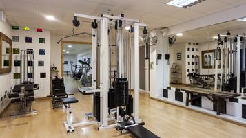 Un gimnasio con diferentes máquinas de ejercicio, un espejo y suelo de madera.