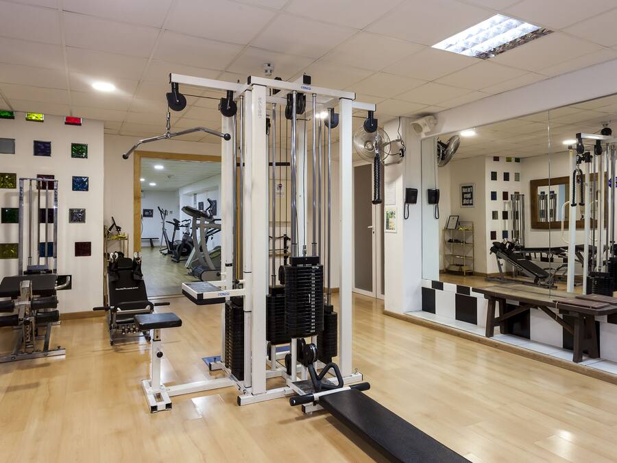 Un gimnasio con diferentes máquinas de ejercicio, un espejo y suelo de madera.