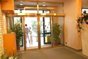 Un hall d’hôtel avec une entrée dotée d’une porte en verre, des plantes en pot et un mur en briques.