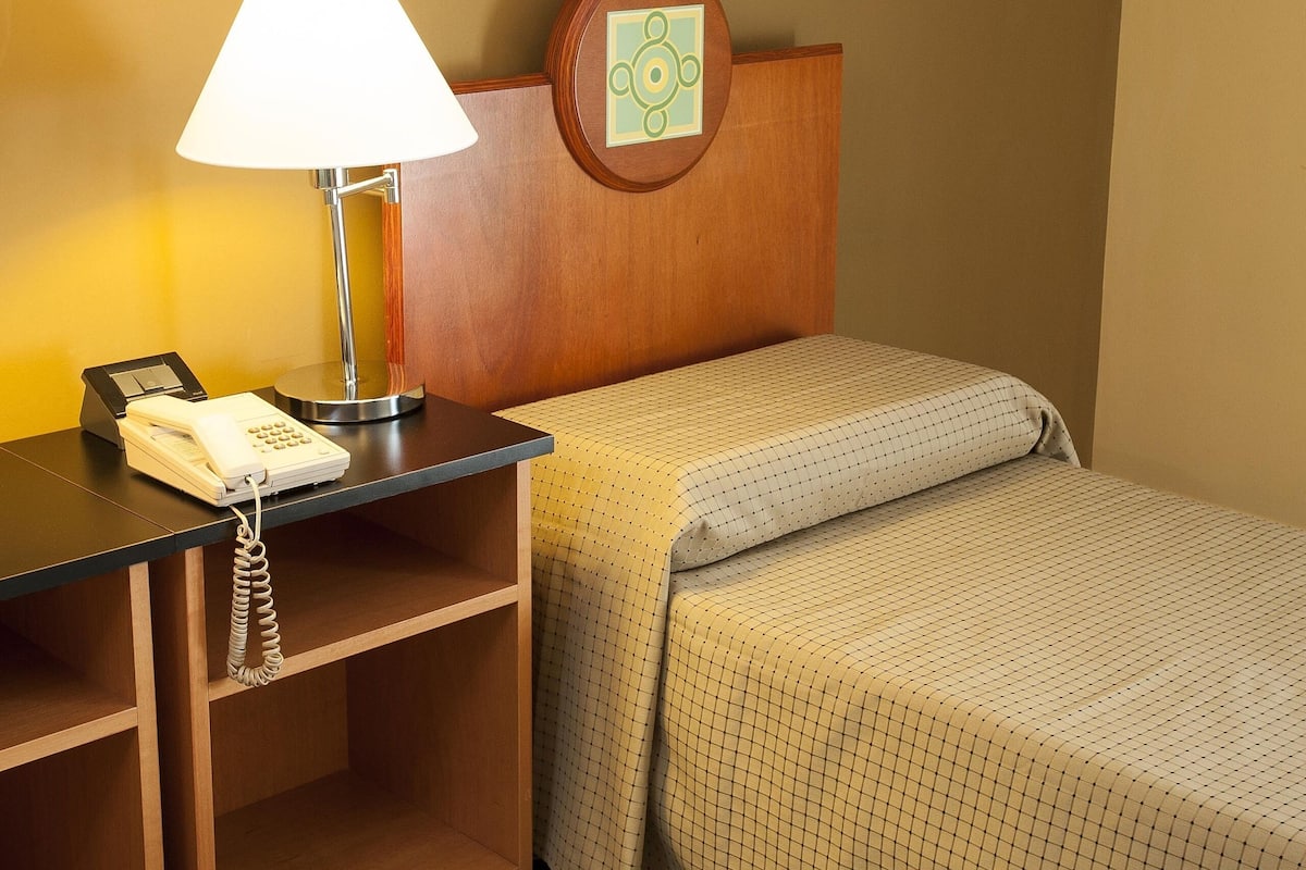 A hotel room with a bed, a nightstand with a lamp, and a telephone.