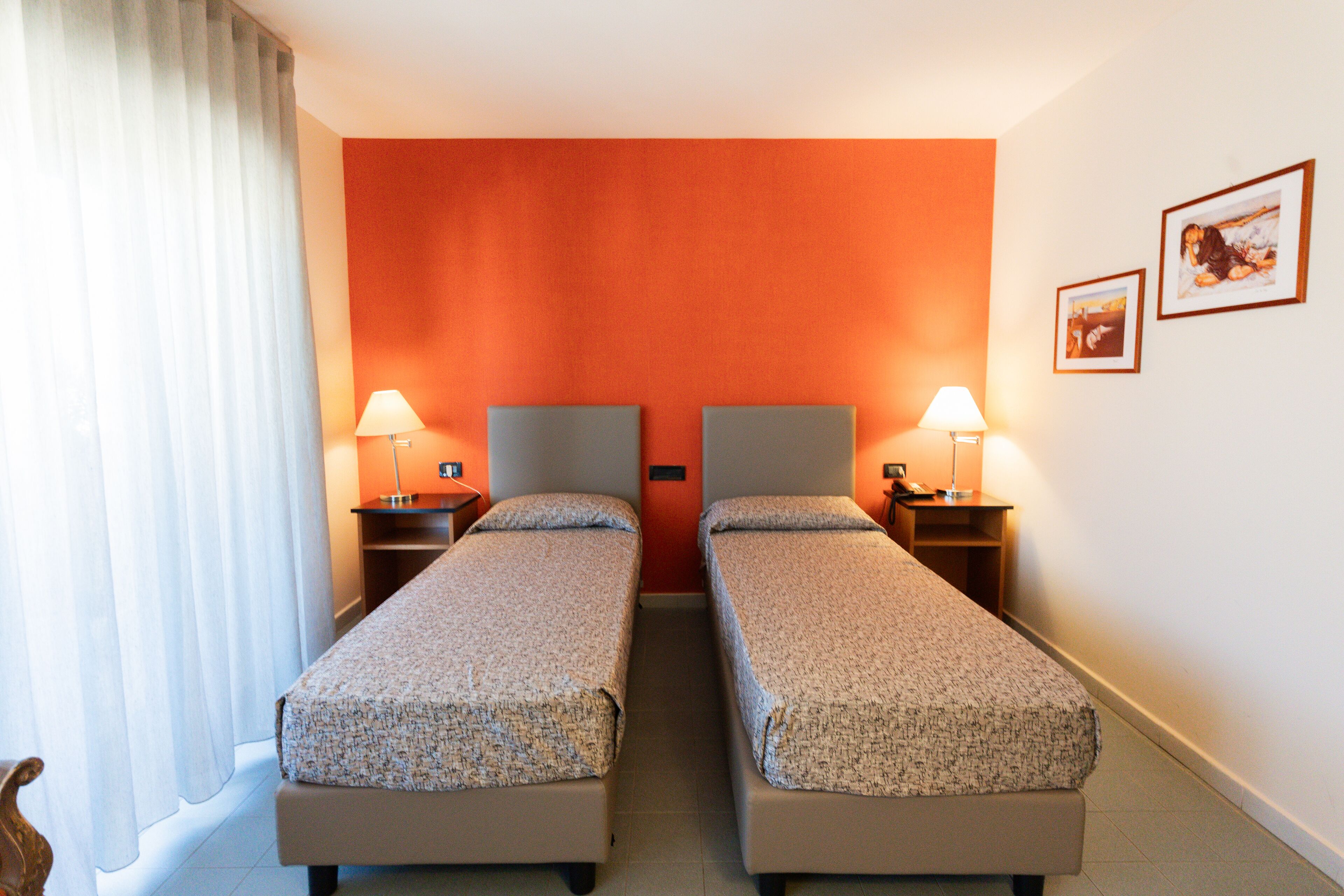 Une chambre d’hôtel avec deux lits simples, une table de chevet avec une lampe et un mur orné de deux tableaux encadrés.