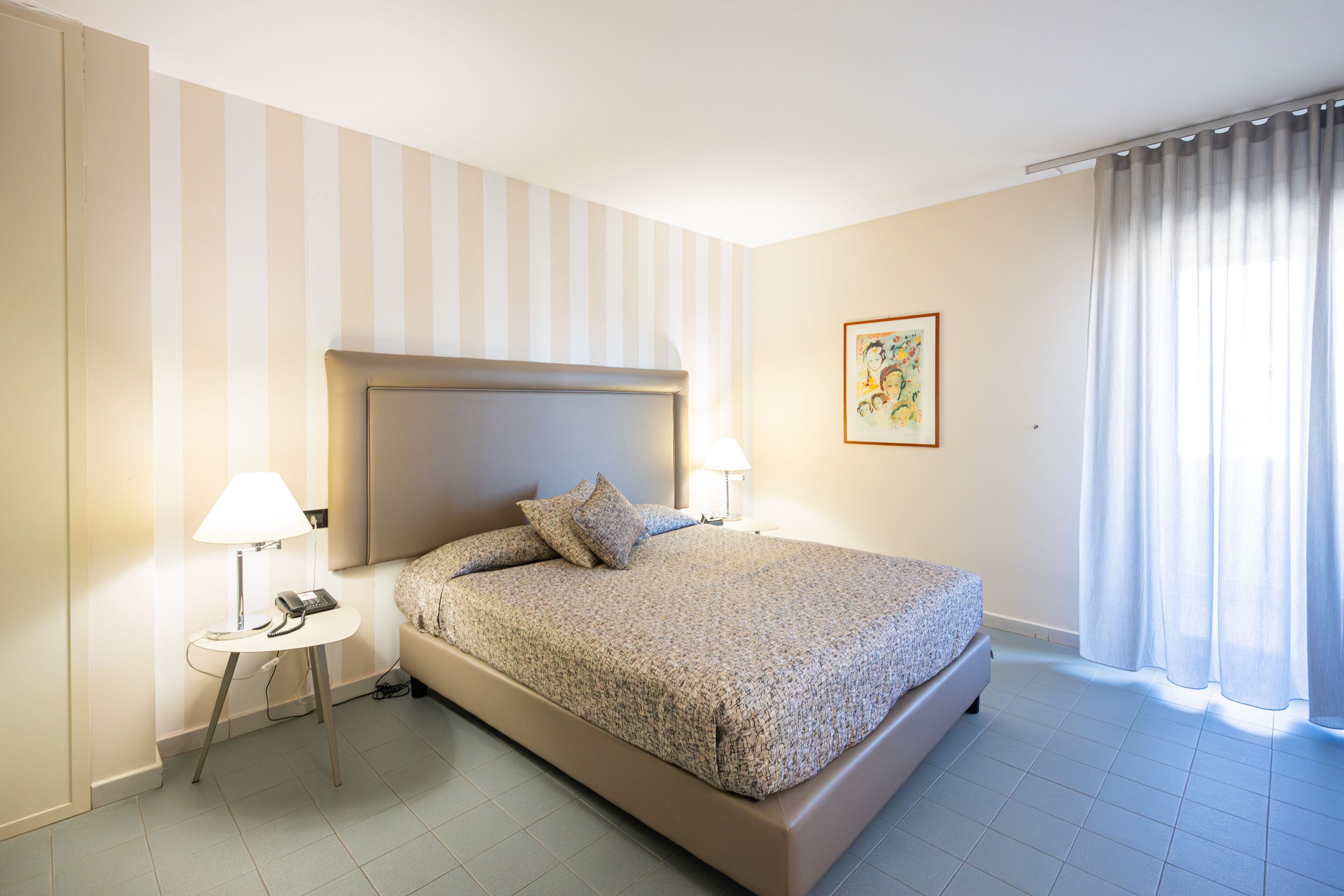 Una camera d'albergo con un letto grande, due lampade sui comodini, un telefono e un quadro appeso al muro.