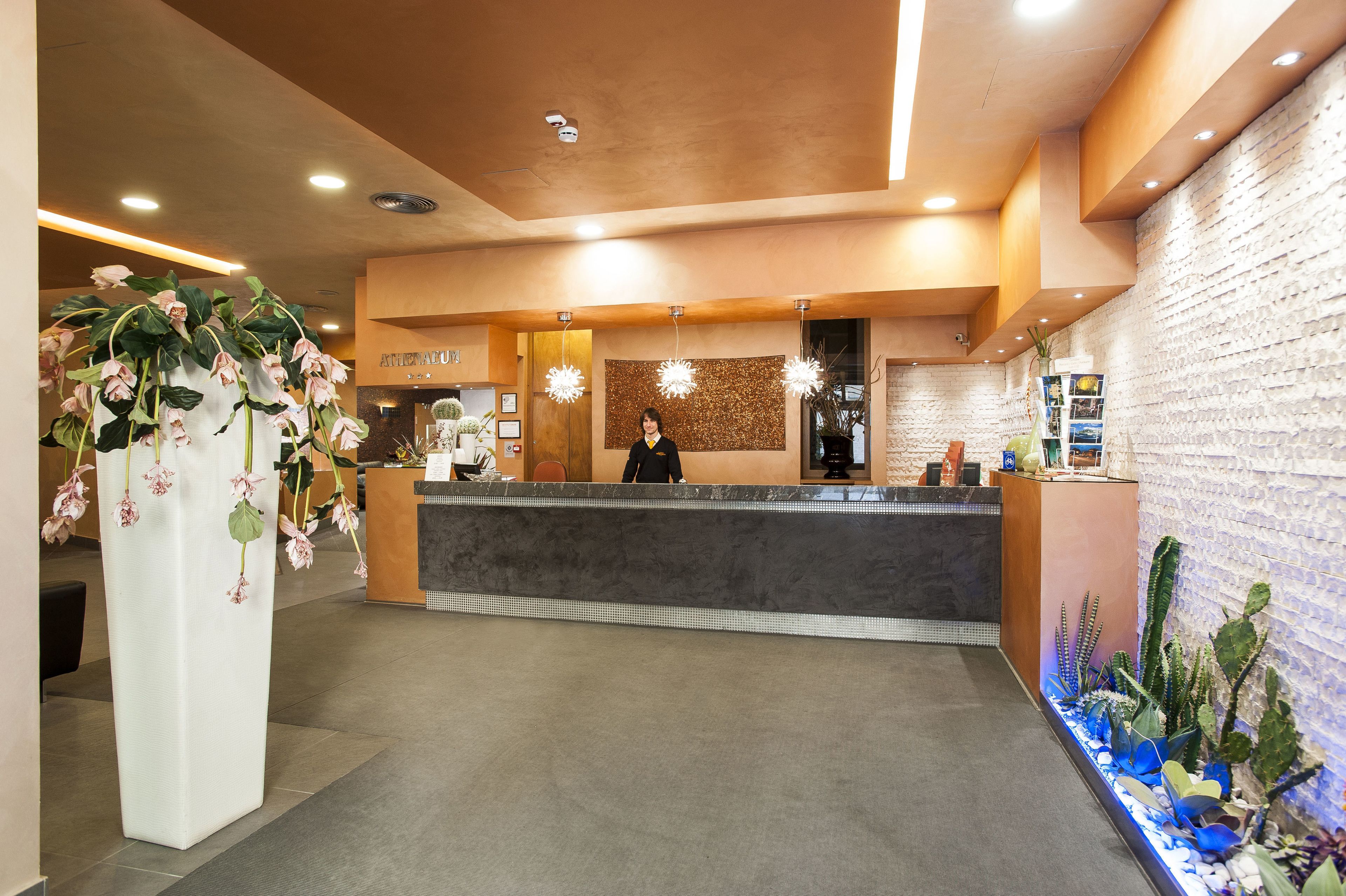 A reception area with a receptionist, a reception desk, and a wall with a textured pattern.