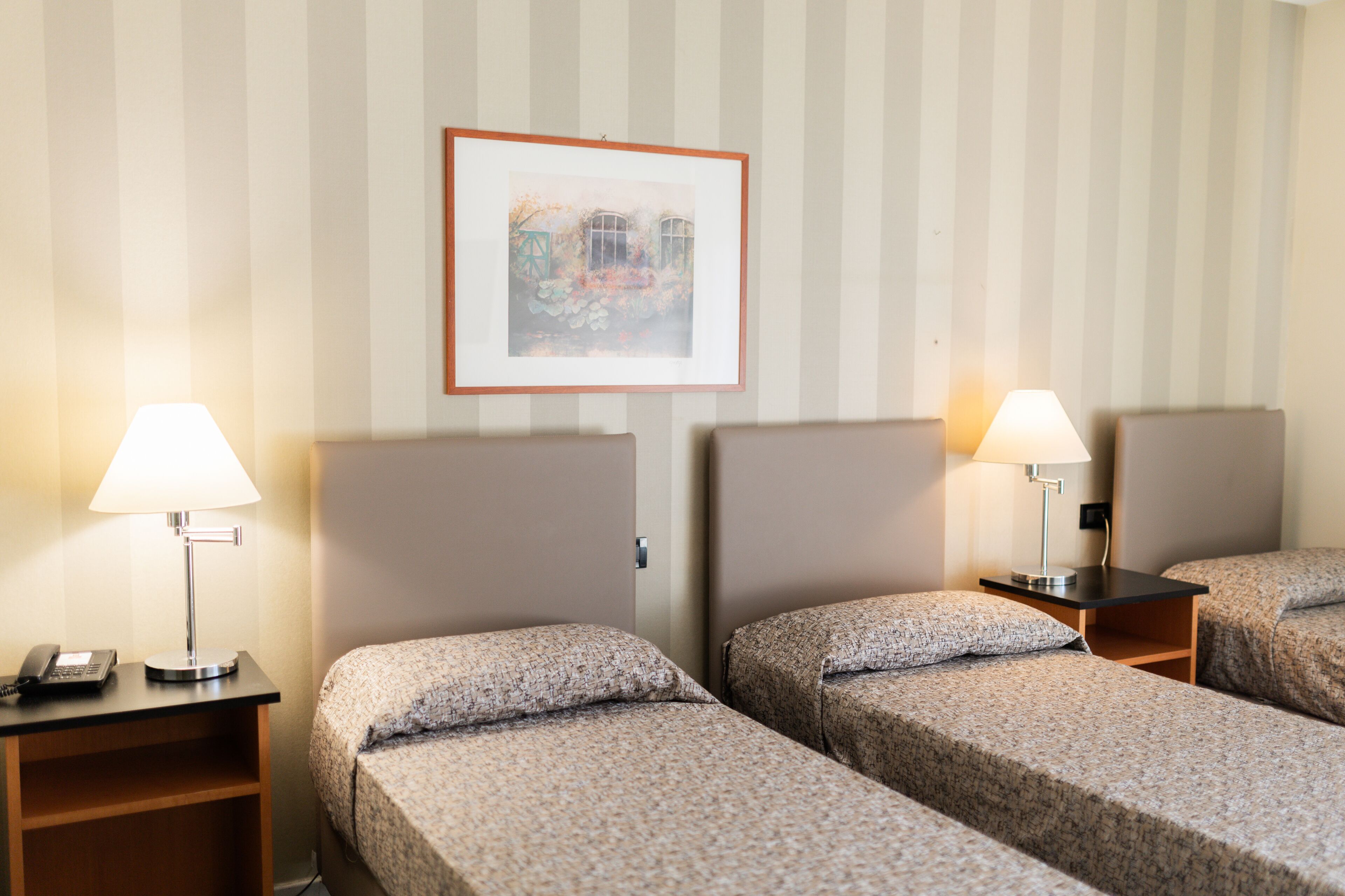 Habitación de hotel con dos camas, cada una con una almohada y una mesita de noche con lámpara y teléfono.