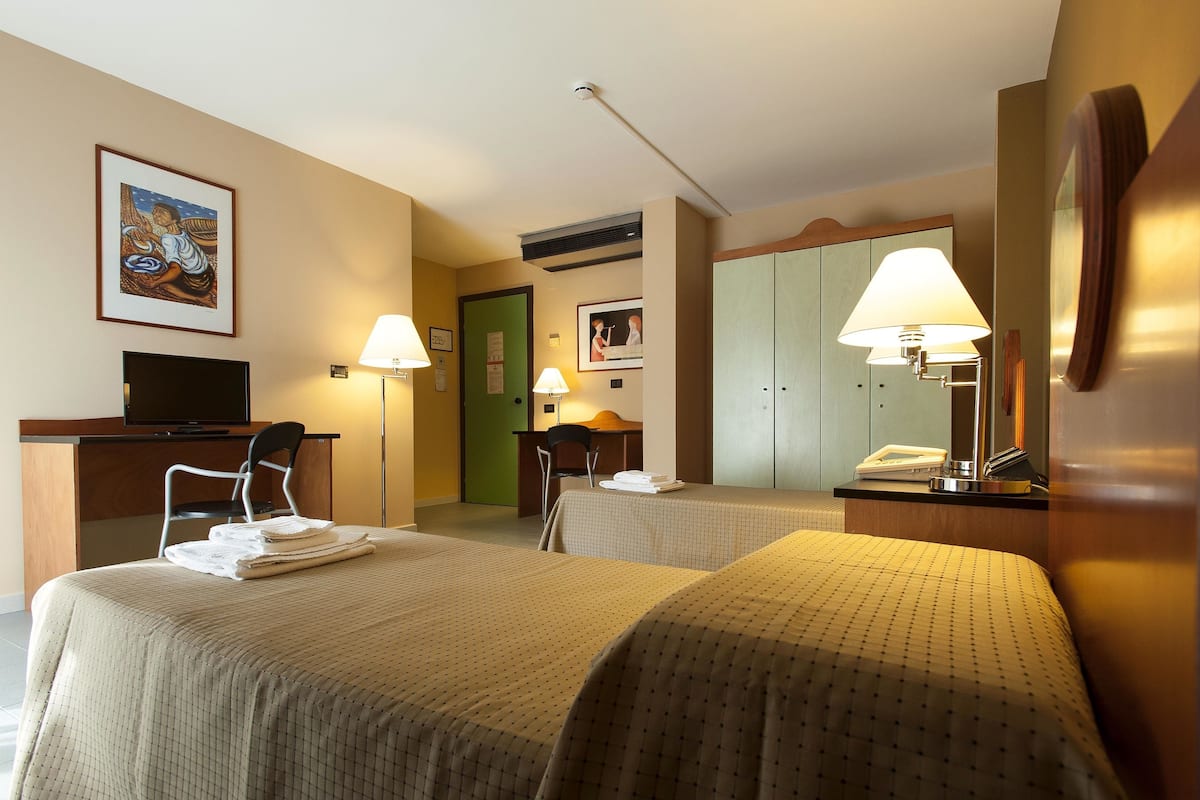 A hotel room with two beds, a desk with a chair, a television, and a lamp.