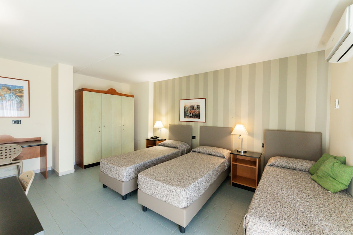 A hotel room with two single beds, a desk, a chair, a wardrobe, and a framed picture on the wall.