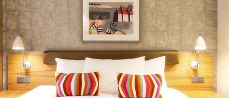 A hotel room with a large bed, two bedside lamps, and a framed artwork on the wall.