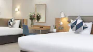 A hotel room with two beds, a desk, a chair, and a small table.