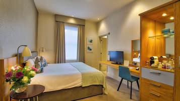 Quarto de hotel com cama, escrivaninha, cadeira, televisão e espelho.
