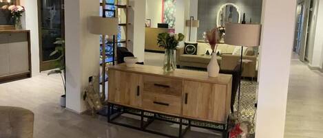 A modern living room with a wooden console table, a sofa, and a coffee table. There is a large mirror above the sofa and a lamp on the console table.