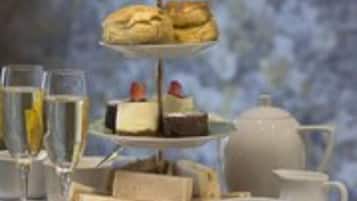 A tiered dessert stand with pastries and a teapot on a table.
