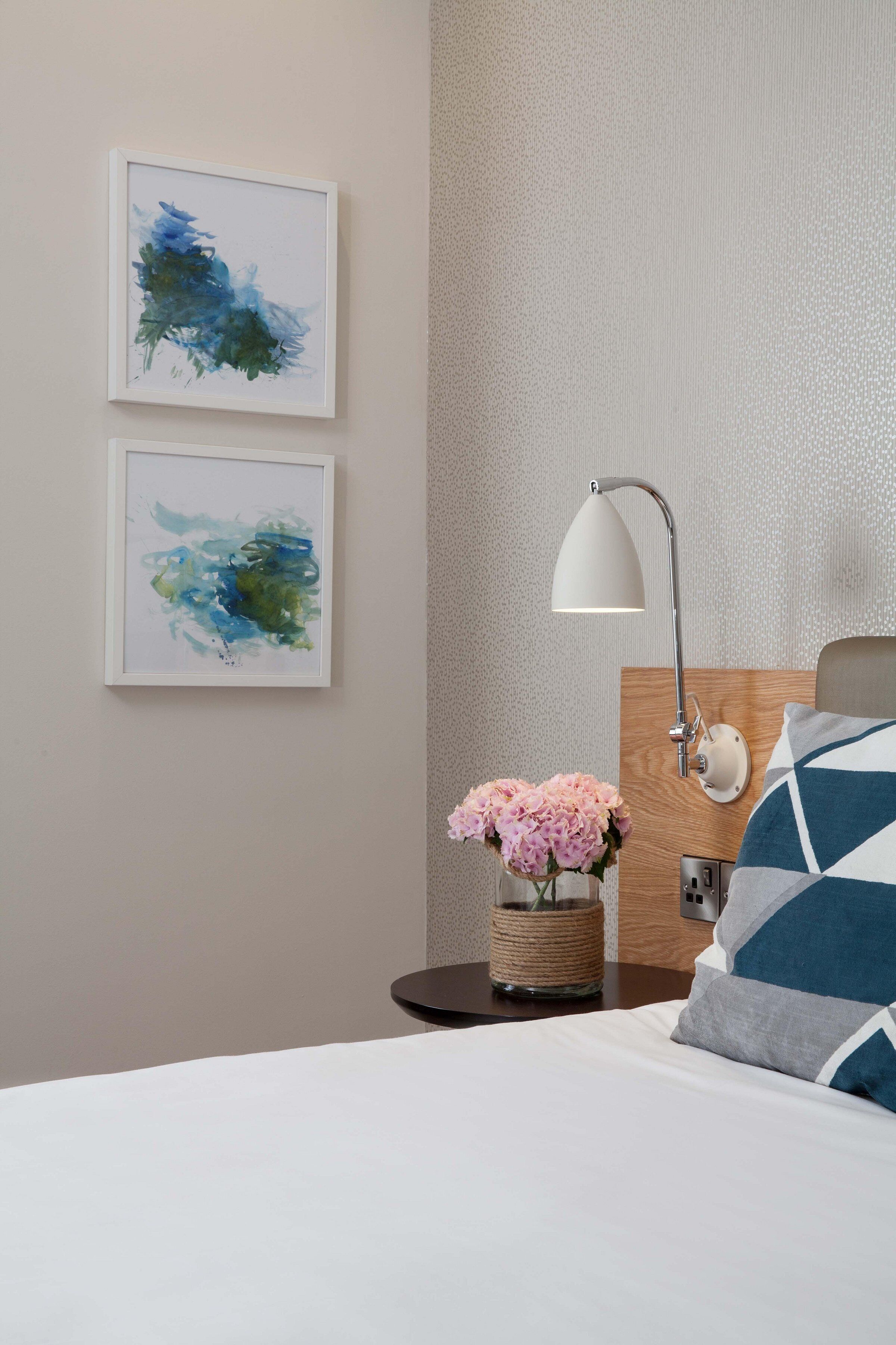 A neatly arranged hotel room with a bed, a bedside table with a lamp, and two abstract paintings on the wall.