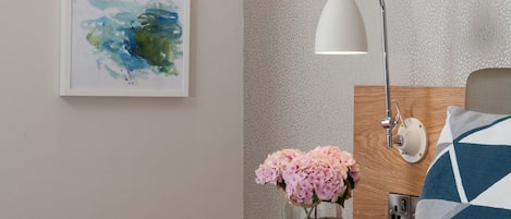 A neatly arranged hotel room with a bed, a bedside table with a lamp, and two abstract paintings on the wall.